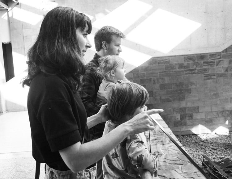 Photographie en noir et blanc d'une famille de deux parents et deux enfants qui regarde l'ancien quai et la barque dans le Hall du Musée.