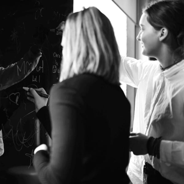 Deux jeunes femmes écrivent sur un tableau noir.