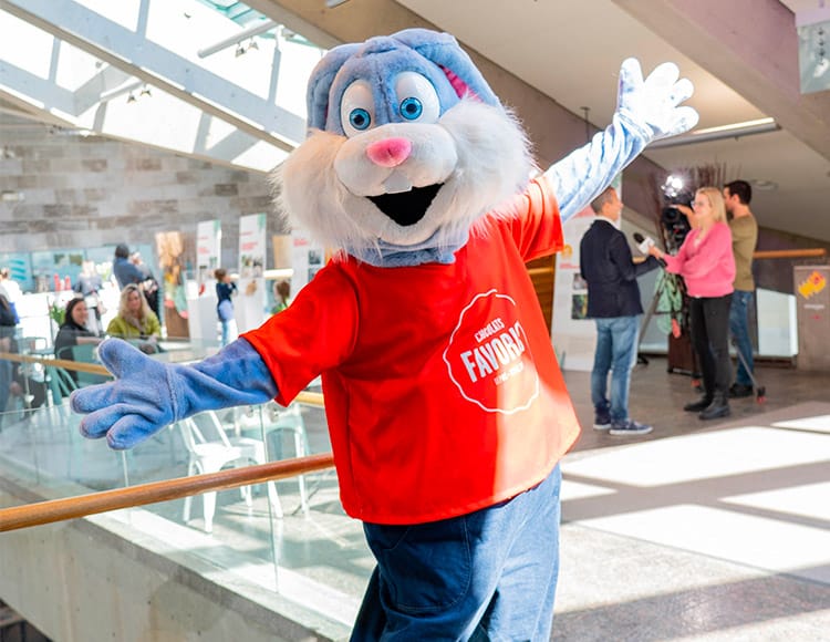 Mascotte de lapin gris portant un chandail à manches courtes rouge avec le logo de Chocolats favoris.