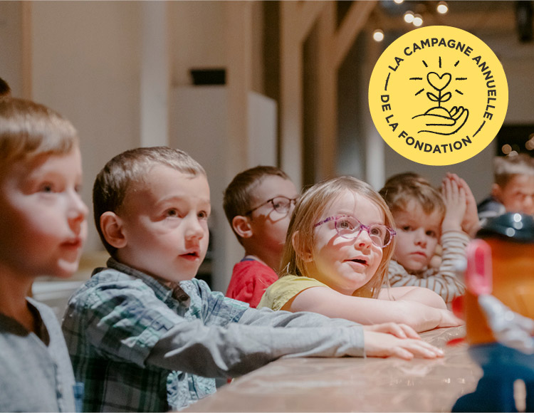 De jeunes enfants sont assis autour d'une table au Musée devant un Monsieur Patate et regarde une personne qui n'est pas sur la photo.