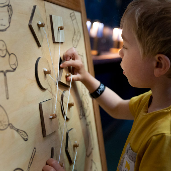 Petit garçon aux cheveux blonds portant un chandail jaune joue avec un jeu en bois dans l'exposition jeunesse Ma maison