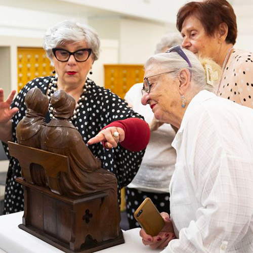 Trois dames âgées regarde une sculpture en bois d'un couple sur un banc