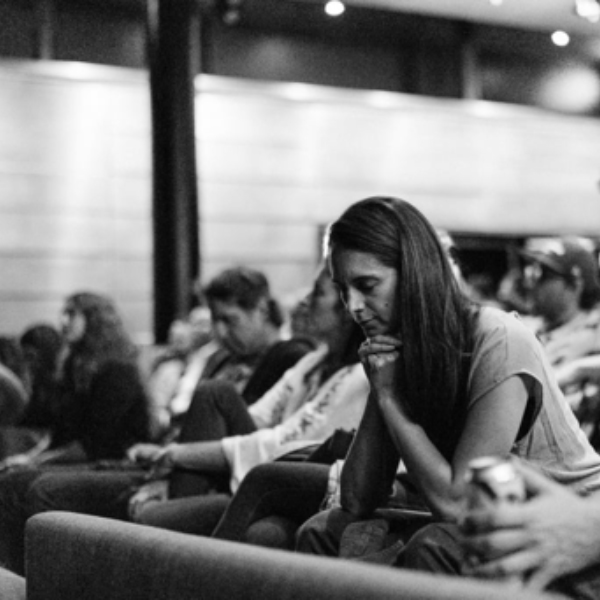 Photo en noir et blanc de plusieurs personnes assis dans une salle et qui écoutent